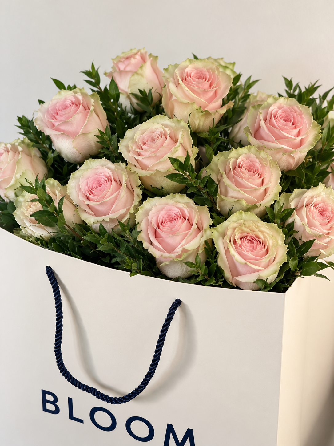 Blush pink garden-style roses with soft ivory and pale green outer petals, arranged with fresh greenery in an elegant Bloommood bouquet.